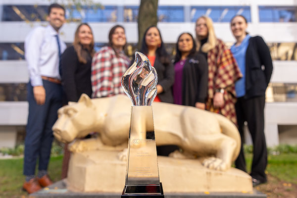 A group of individuals standing in front of a Penn State Nittany Lion statue with an award sitting on the ground in front of the status.