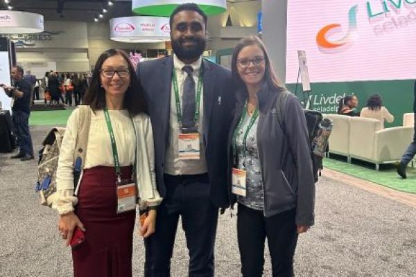 Dr. Nataliya Smith, Dr. Theja Channapragada and Breianna Hummer-Bair stand in the center of a conference center surrounded by exhibits.