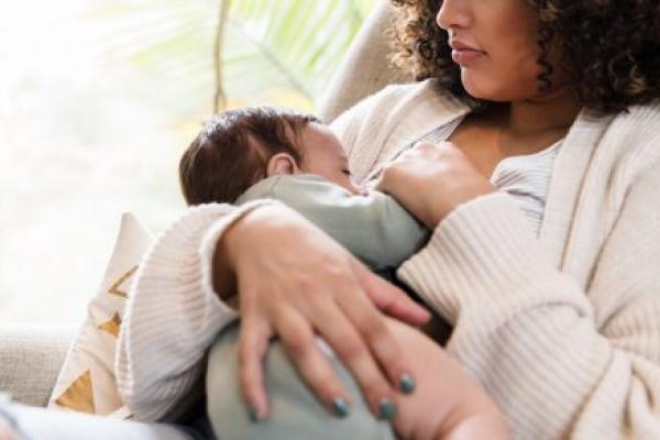 A woman sits in a chair, breastfeeding her infant child.