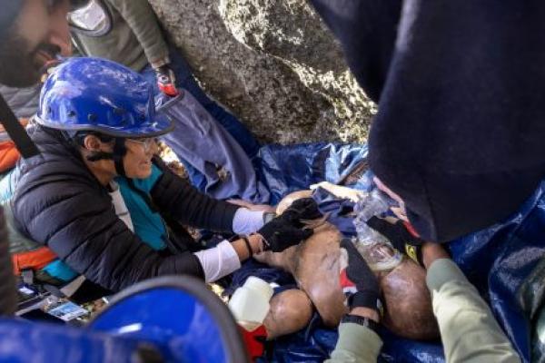 Students practice a simulated rope rescue next to climbing rocks with a mannequin