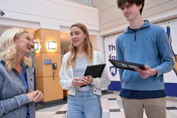 A female nurse speaks to a female and male high school student. The students are holding awards for performing life-saving actions.