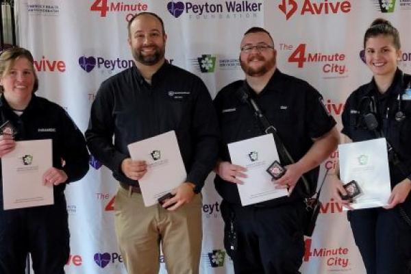 Four people pose for a photograph, each holding in front of them certificates of recognition.