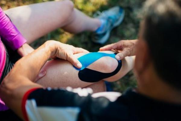 Mature man applying bandage on knee of his wife outdoor.