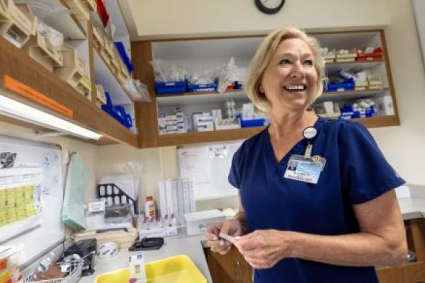 A pharmacist at Penn State Health's Holy Spirit Medical Center, stands smiling in the pharmacy, surrounded by shelves of medical supplies and charts.