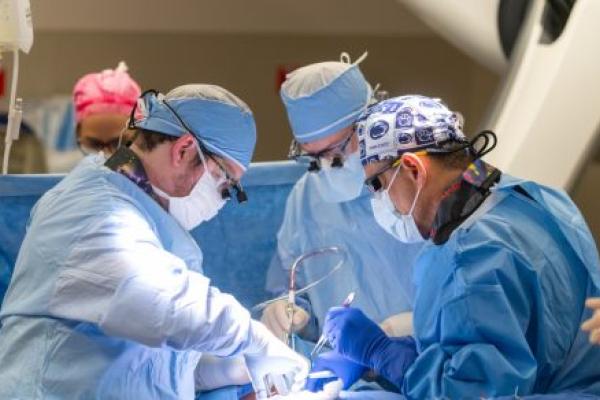 Two doctors perform a transcarotid artery revascularization procedure at Penn State Health St. Joseph Medical Center. They are focused and working in a well-lit operating room, using medical instruments and equipment to carry out the procedure.