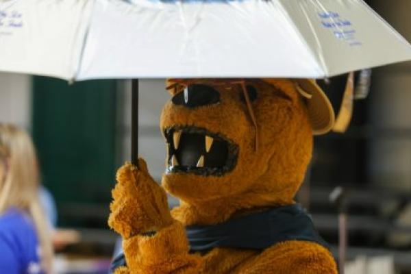 Someone dressed as the Penn State Nittany Lion raises an umbrella.