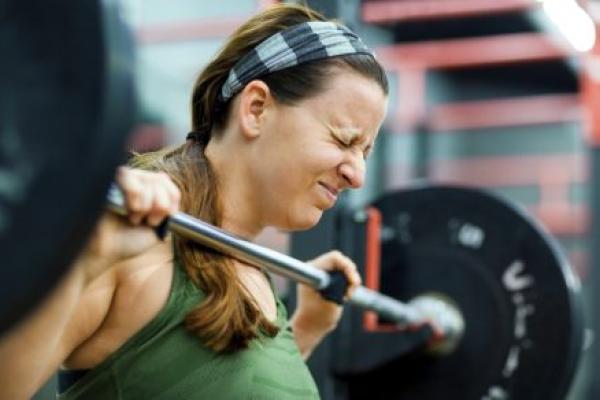 A woman closes her eyes as she lifts a heavy weight off of a rack at a gym.