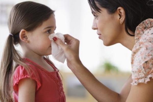 A mother wipes her daughter’s nose with a tissue.