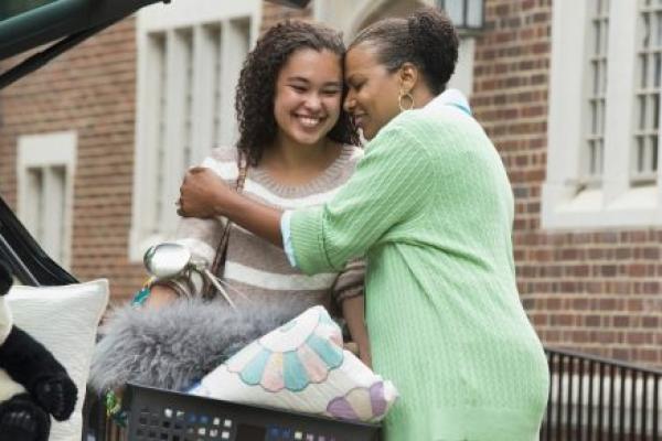 A mother and daughter hug near a car.