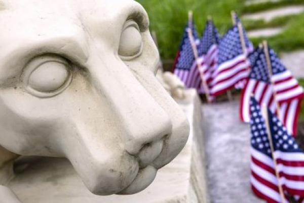 The head of a Nittany Lion statue with small American flags stuck in the ground beside it.