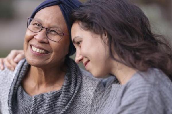 A younger woman embraces a senior woman with her right arm.