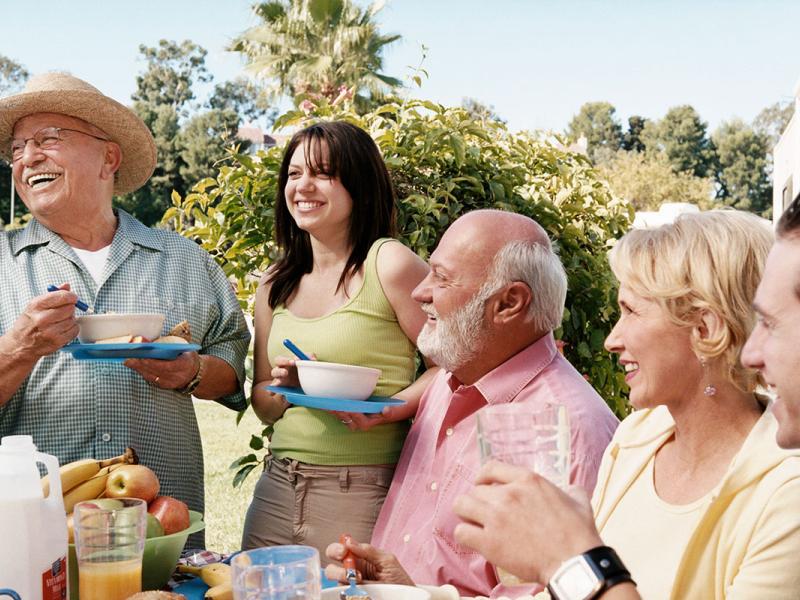 Grandparents and Grandchildren Stand at a Breakfast Table Outdoors By a Motor Home, Laughing