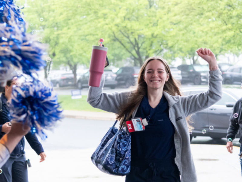 A person in scrubs and a cardigan walks through a crowd of Penn State cheerleaders with their arms up victoriously