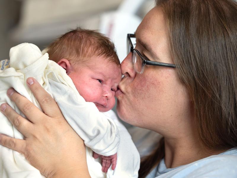 A woman lovingly kisses her newborn baby in a hospital setting, capturing a tender moment of maternal affection.