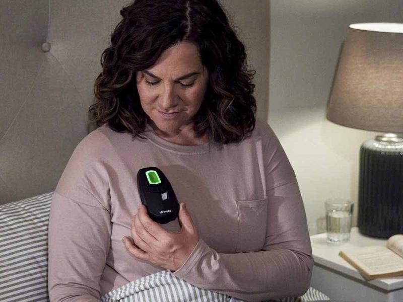 A patient is seated upright in bed holding the Inspire sleep remote to her chest to activate the therapy.